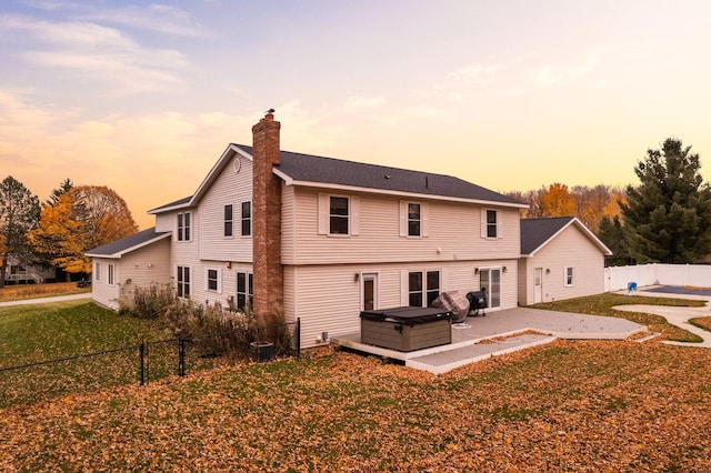 back house at dusk featuring a yard, a patio, and a hot tub