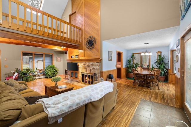 living room with wood walls, high vaulted ceiling, a fireplace, wood-type flooring, and a notable chandelier