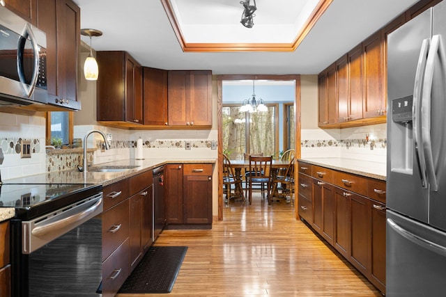 kitchen with sink, appliances with stainless steel finishes, pendant lighting, a tray ceiling, and light wood-type flooring