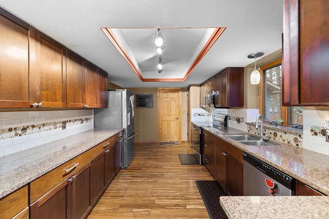 kitchen with sink, appliances with stainless steel finishes, a tray ceiling, light wood-type flooring, and decorative backsplash