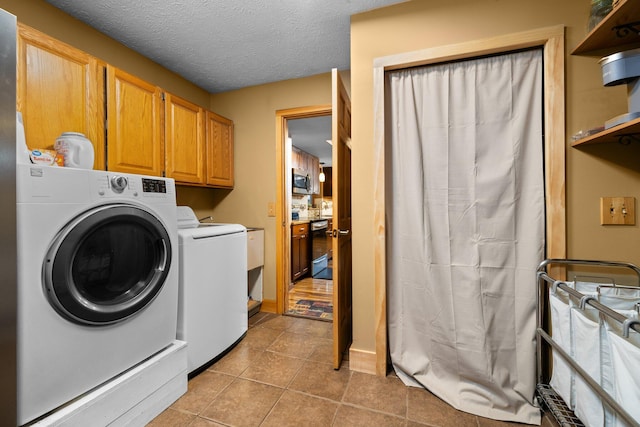 washroom featuring cabinets, washing machine and dryer, a textured ceiling, and light tile patterned floors