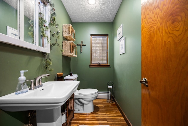 bathroom with sink, a textured ceiling, wood-type flooring, a baseboard heating unit, and toilet