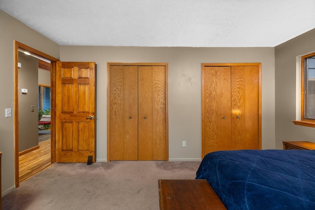 bedroom featuring a textured ceiling, light carpet, and two closets