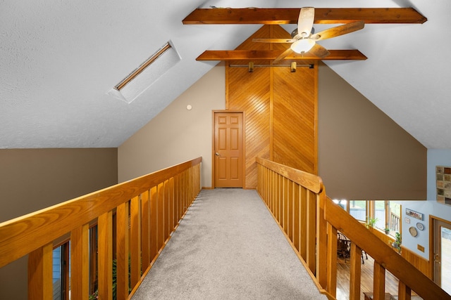 hallway featuring wood walls, vaulted ceiling with skylight, a textured ceiling, and light colored carpet