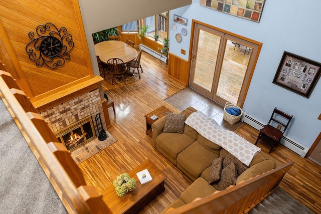 living room with hardwood / wood-style flooring, baseboard heating, wooden walls, and a high ceiling