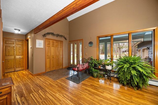 entrance foyer featuring a textured ceiling, light wood-type flooring, baseboard heating, and vaulted ceiling with beams