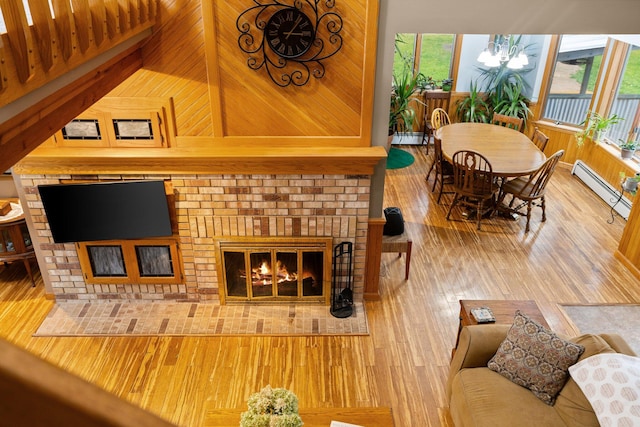 living room with a brick fireplace, baseboard heating, wooden walls, and hardwood / wood-style floors