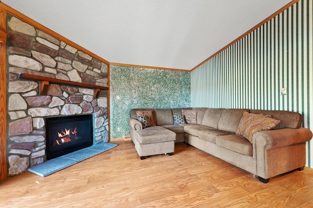 living room featuring light wood-type flooring, ornamental molding, a textured ceiling, vaulted ceiling, and a stone fireplace