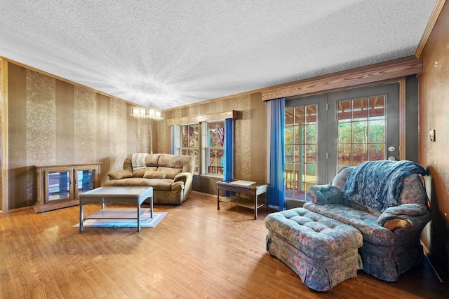 living area with wood-type flooring, a textured ceiling, ornamental molding, and a notable chandelier