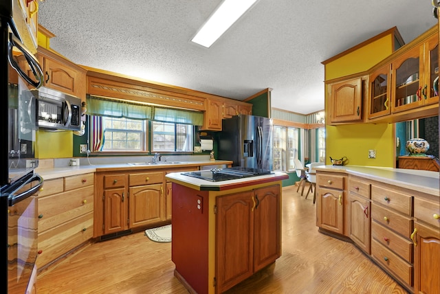 kitchen featuring black appliances, sink, light hardwood / wood-style flooring, a textured ceiling, and a kitchen island