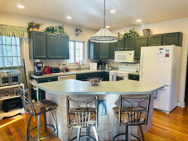 kitchen with a textured ceiling, hanging light fixtures, sink, light hardwood / wood-style floors, and white appliances