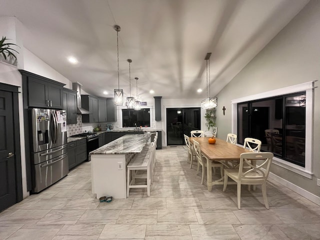 kitchen featuring lofted ceiling, stainless steel fridge, light stone countertops, and a center island