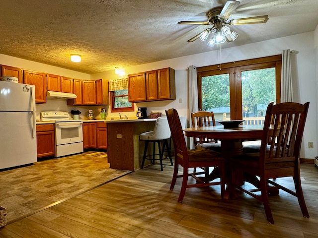 kitchen featuring kitchen peninsula, a textured ceiling, white appliances, a breakfast bar, and light wood-type flooring