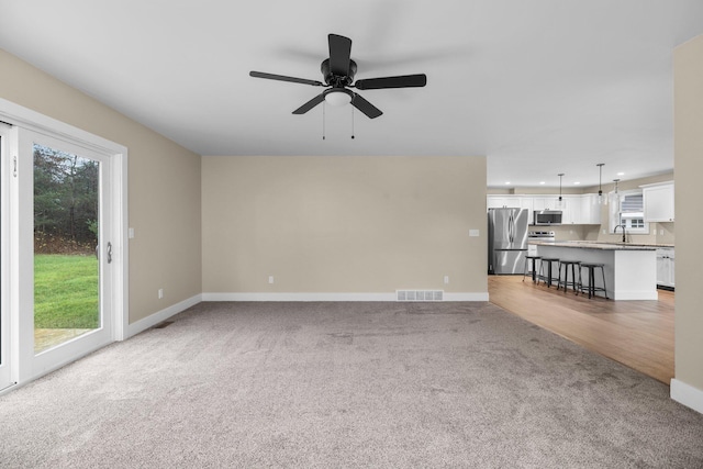 unfurnished living room with carpet, ceiling fan, and sink