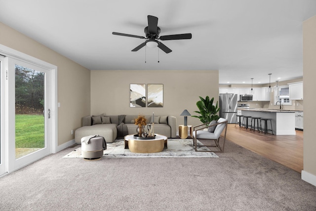 living room with ceiling fan, light colored carpet, and sink