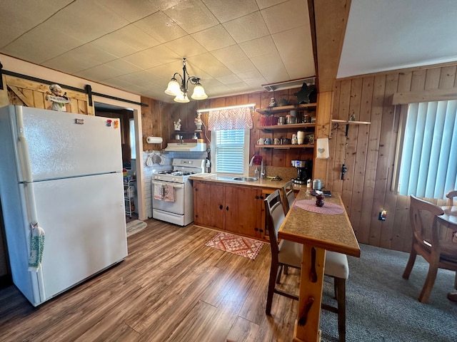 kitchen with white appliances, wooden walls, sink, pendant lighting, and wood-type flooring