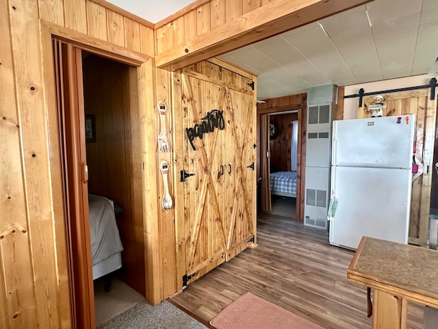 interior space featuring wood walls, white fridge, a barn door, and hardwood / wood-style floors