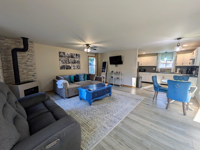 living room featuring a wood stove, ceiling fan, and light hardwood / wood-style floors