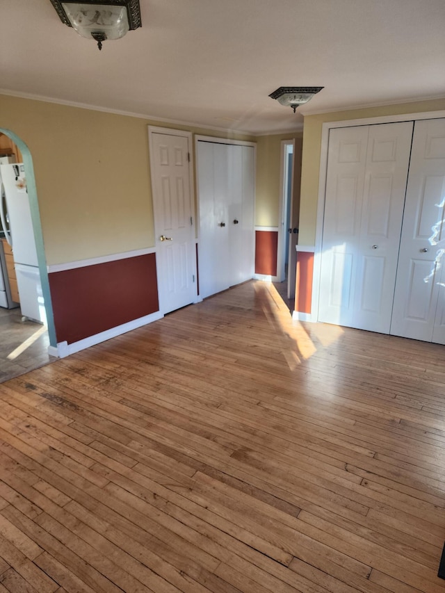 unfurnished bedroom featuring white refrigerator, light hardwood / wood-style floors, crown molding, and multiple closets