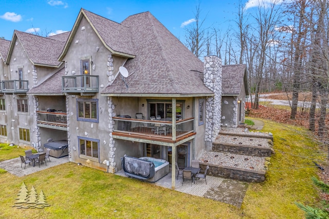 rear view of property featuring a yard, a patio, a balcony, and a hot tub