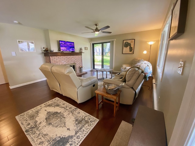 living room featuring dark hardwood / wood-style floors, ceiling fan, and a brick fireplace