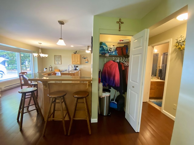 kitchen featuring a kitchen breakfast bar, ceiling fan with notable chandelier, dark hardwood / wood-style floors, decorative light fixtures, and kitchen peninsula