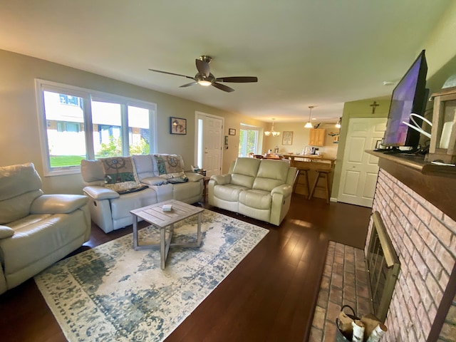 living room featuring ceiling fan with notable chandelier, dark hardwood / wood-style floors, and a brick fireplace