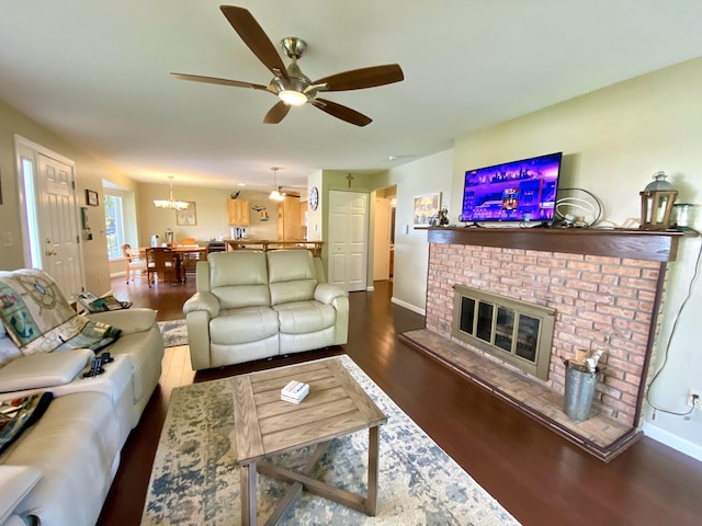 living room featuring a fireplace, dark wood-type flooring, and ceiling fan with notable chandelier