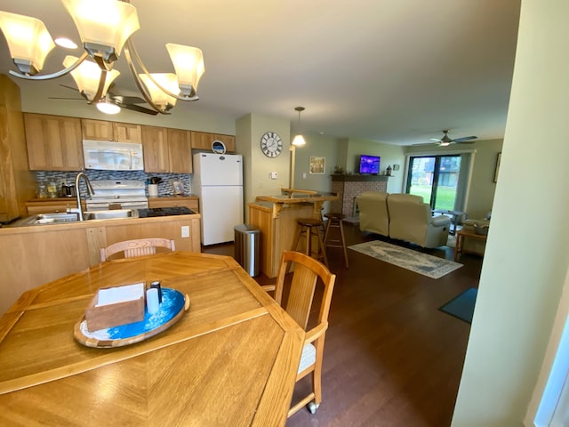 dining area featuring ceiling fan with notable chandelier, a fireplace, dark hardwood / wood-style flooring, and sink