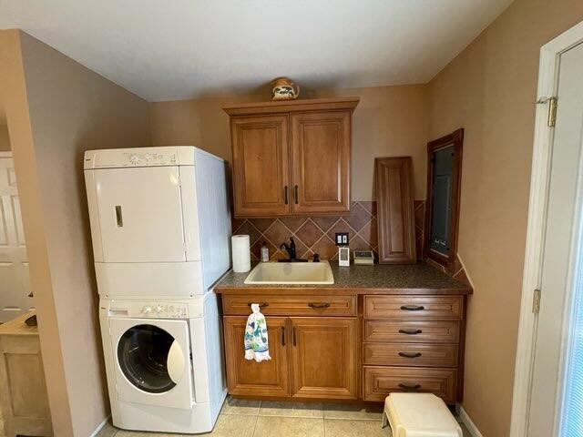 clothes washing area featuring sink, light tile patterned floors, and stacked washer and clothes dryer