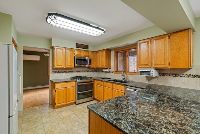 kitchen featuring backsplash, a baseboard heating unit, sink, appliances with stainless steel finishes, and kitchen peninsula