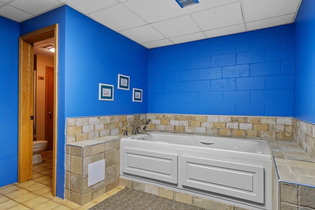 bathroom featuring tile patterned floors, a bathing tub, a drop ceiling, and toilet