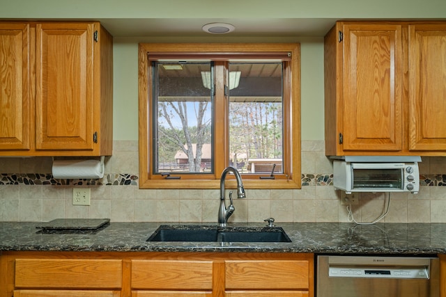 kitchen with backsplash, dark stone countertops, dishwasher, and sink