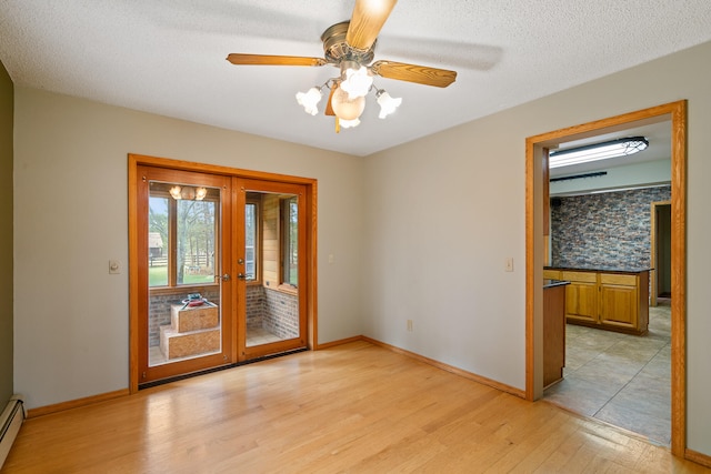 spare room featuring ceiling fan, french doors, light hardwood / wood-style flooring, a baseboard heating unit, and a textured ceiling