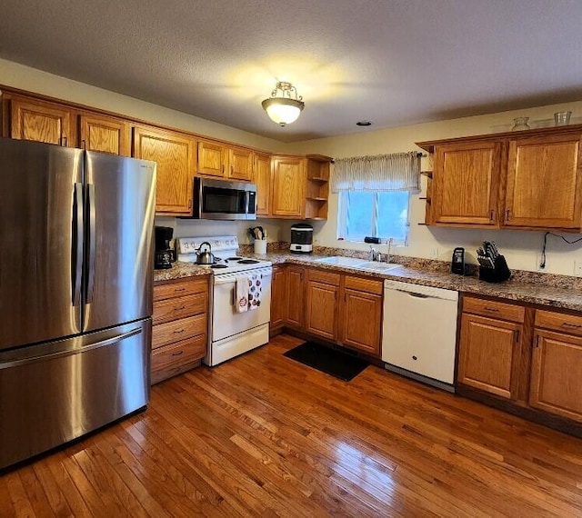 kitchen with sink, dark stone countertops, a textured ceiling, appliances with stainless steel finishes, and dark hardwood / wood-style flooring