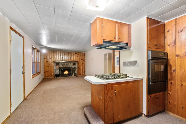 kitchen featuring light carpet, stainless steel gas cooktop, wooden walls, a fireplace, and black oven