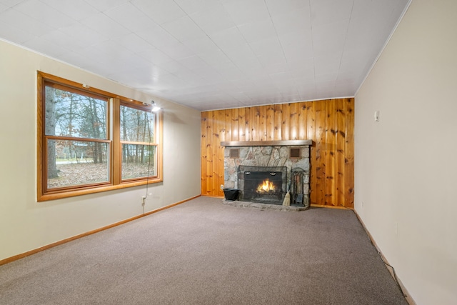 unfurnished living room featuring wood walls, a stone fireplace, and carpet floors