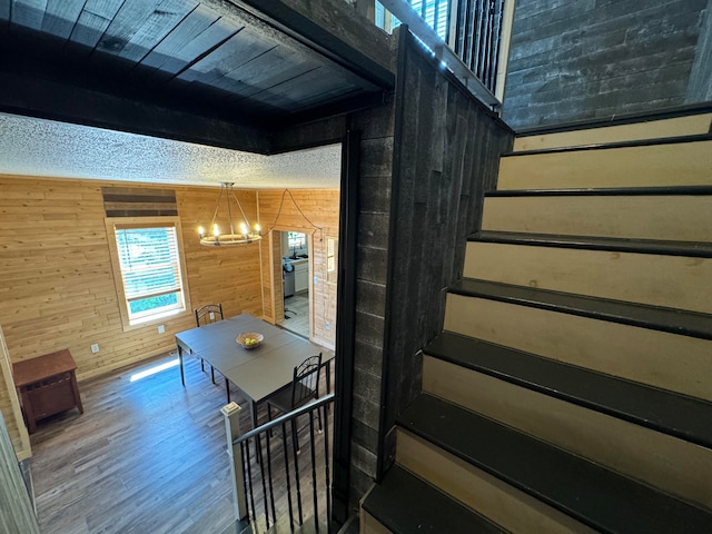 stairs featuring hardwood / wood-style floors, a notable chandelier, and wood walls