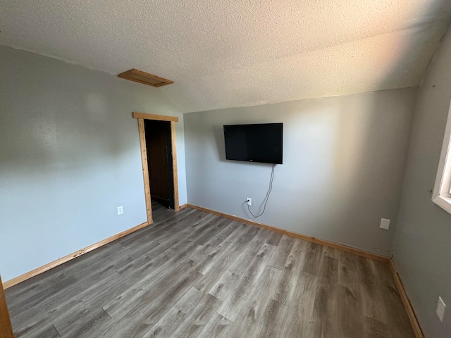 spare room with vaulted ceiling, light hardwood / wood-style flooring, and a textured ceiling