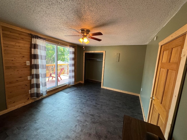 unfurnished bedroom with access to exterior, ceiling fan, a closet, and wood walls