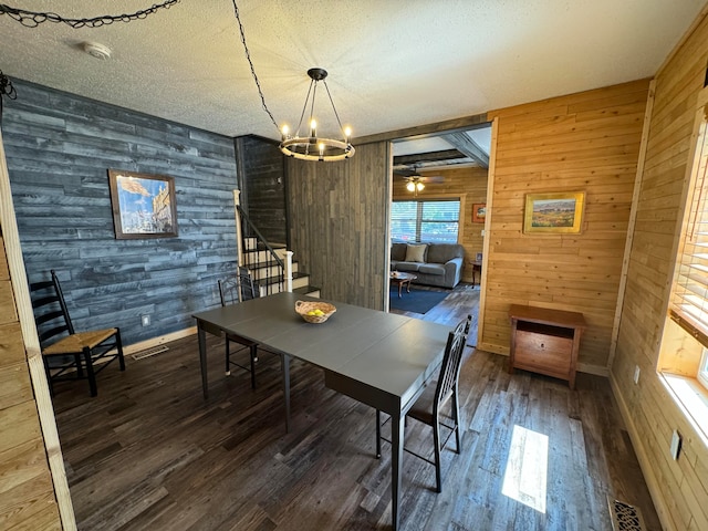 dining area with ceiling fan with notable chandelier, wood walls, dark hardwood / wood-style flooring, and a textured ceiling