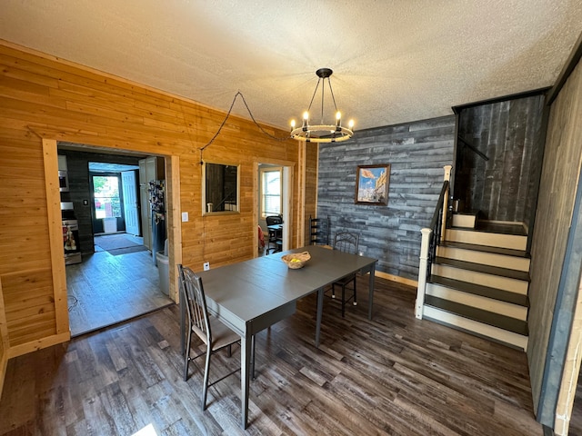 dining room featuring a textured ceiling, dark hardwood / wood-style floors, an inviting chandelier, and wooden walls