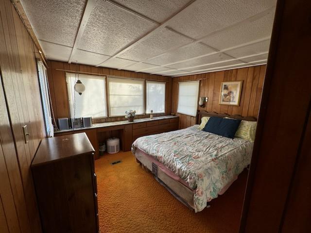 carpeted bedroom featuring a paneled ceiling and wooden walls