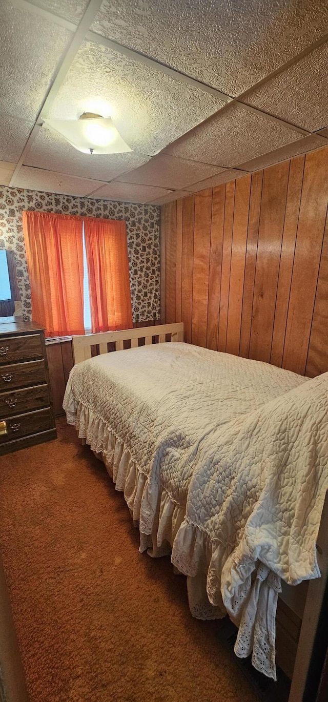 carpeted bedroom featuring a paneled ceiling and wood walls