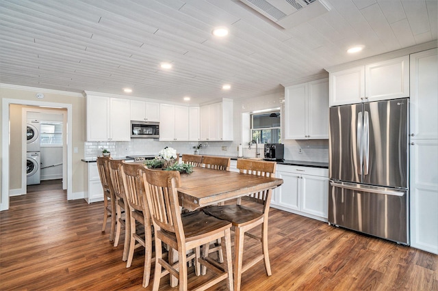 kitchen featuring stainless steel appliances, tasteful backsplash, stacked washer and clothes dryer, and dark hardwood / wood-style flooring