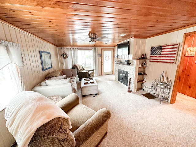 carpeted living room featuring ceiling fan, wood ceiling, a fireplace, and wooden walls