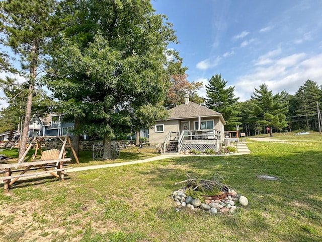 back of house featuring a deck, an outdoor fire pit, and a lawn