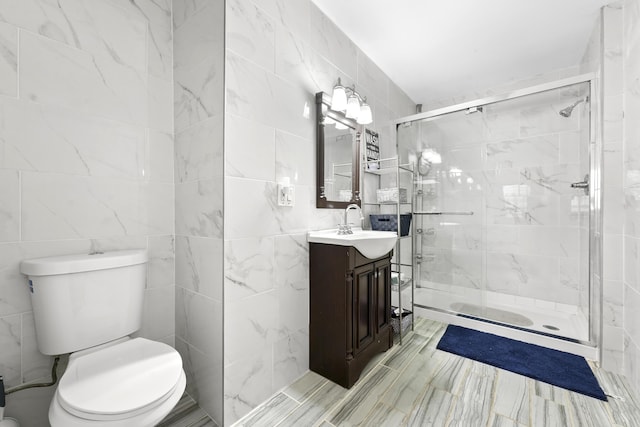 bathroom featuring a shower with door, vanity, tile walls, and toilet