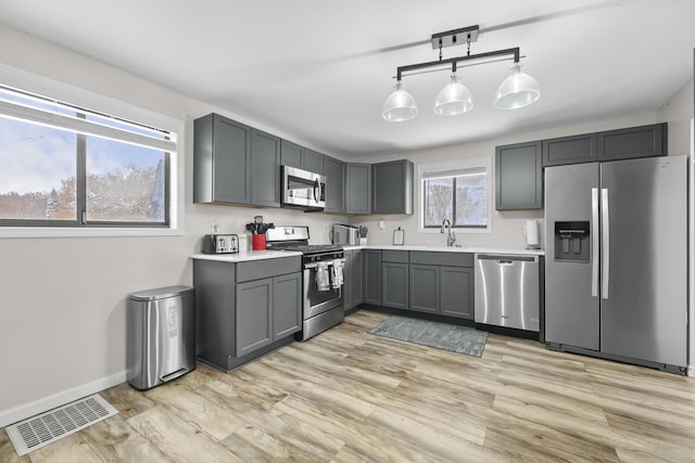 kitchen with gray cabinets, pendant lighting, stainless steel appliances, and light hardwood / wood-style floors