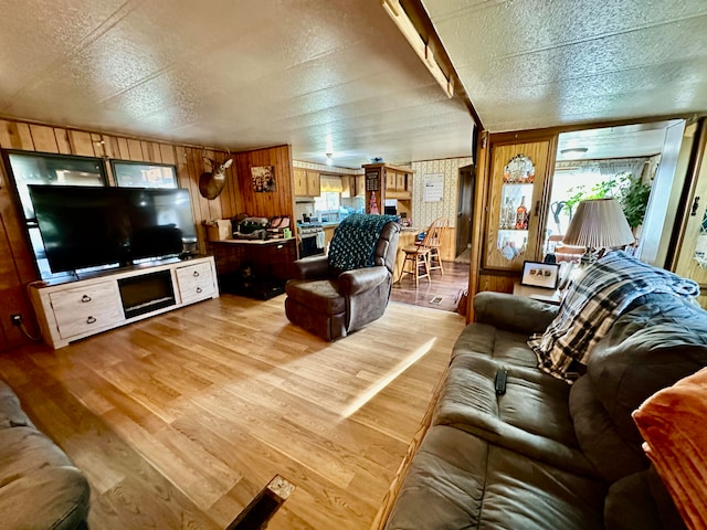 living room with light hardwood / wood-style floors, a textured ceiling, and wooden walls